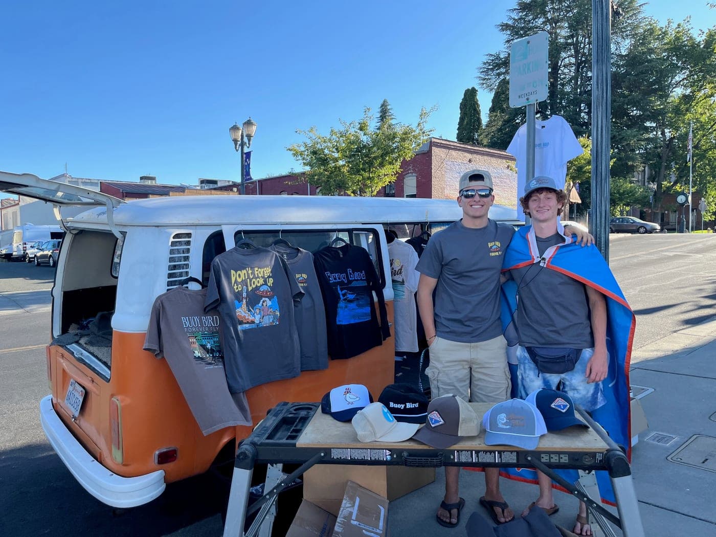 Buoy Bird merch booth with an orange bus and shirts